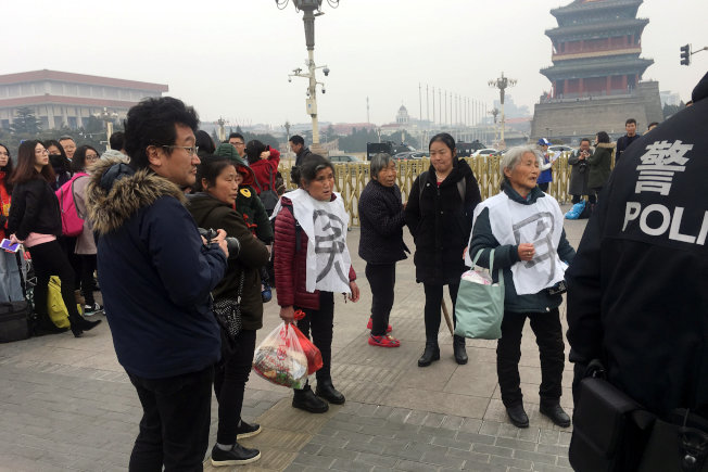 警察拦截两名在天安门广场穿着“冤”字衣服的妇人,周遭有许多民众围观。(路透)